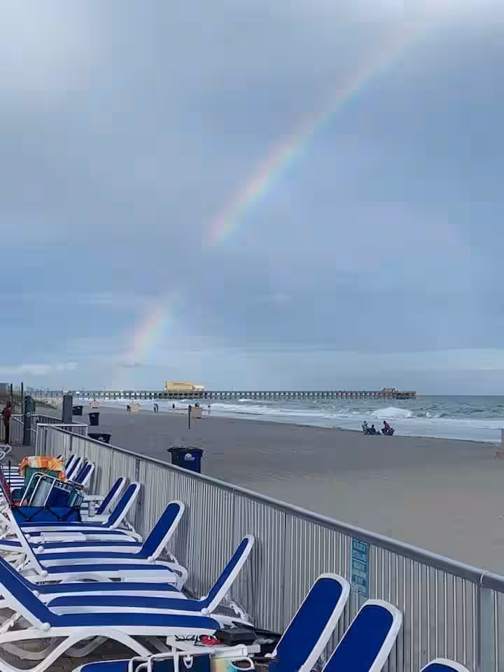 Loungers on the oceanfront deck with a rainbow over the beach and Apache Pier
