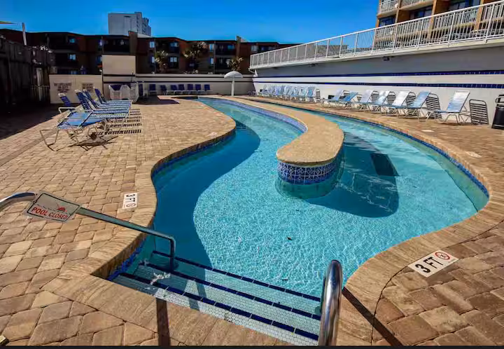 Curved resort pool and lazy river with lounge chairs on the paver deck