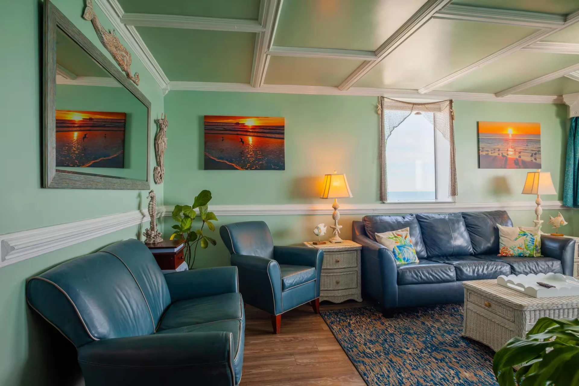 Coastal living room with leather seating, green walls, coffered ceiling, and beach sunset artwork